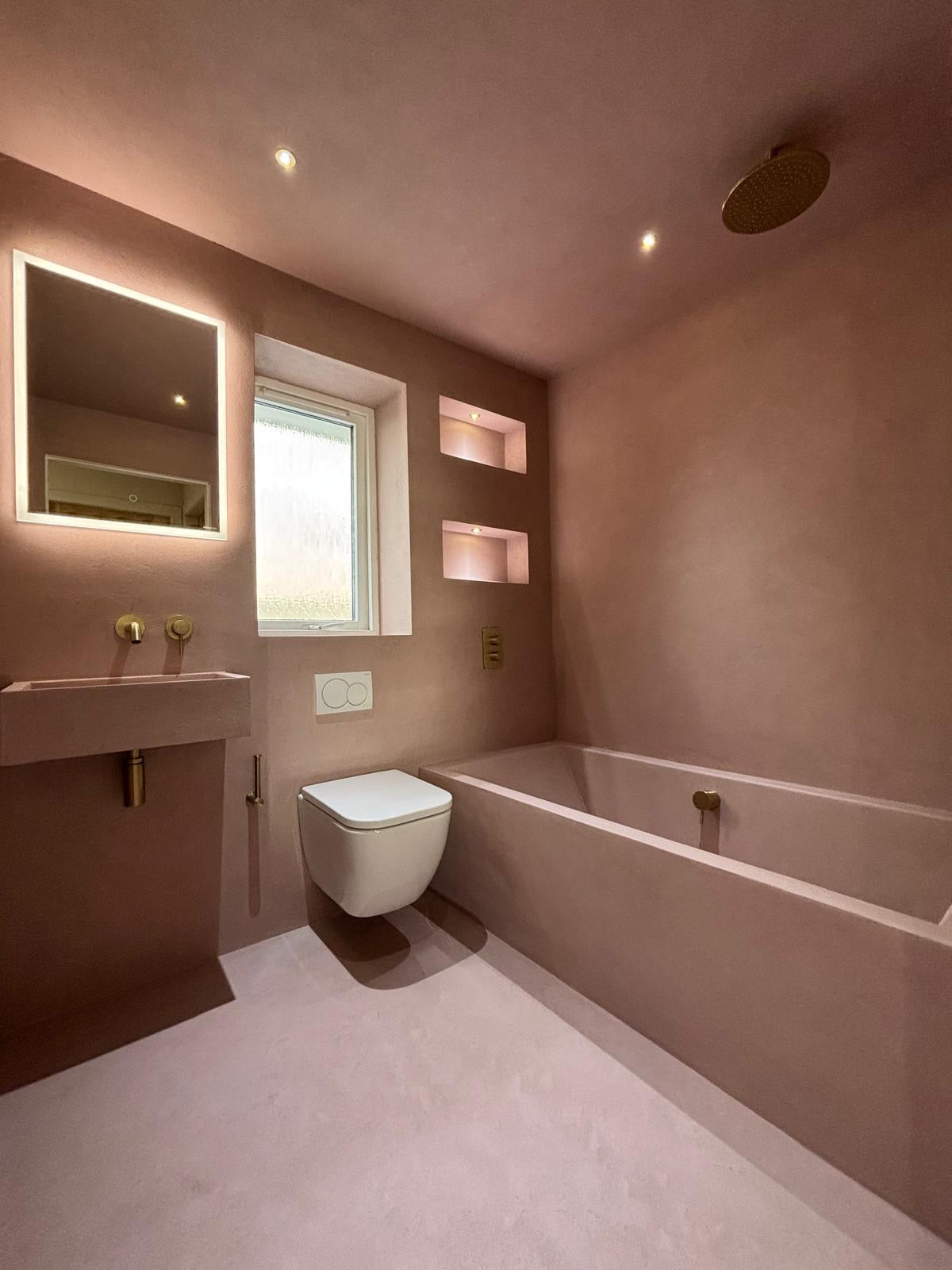 Modern bathroom with pink walls, a microcement bathtub, and sink.
