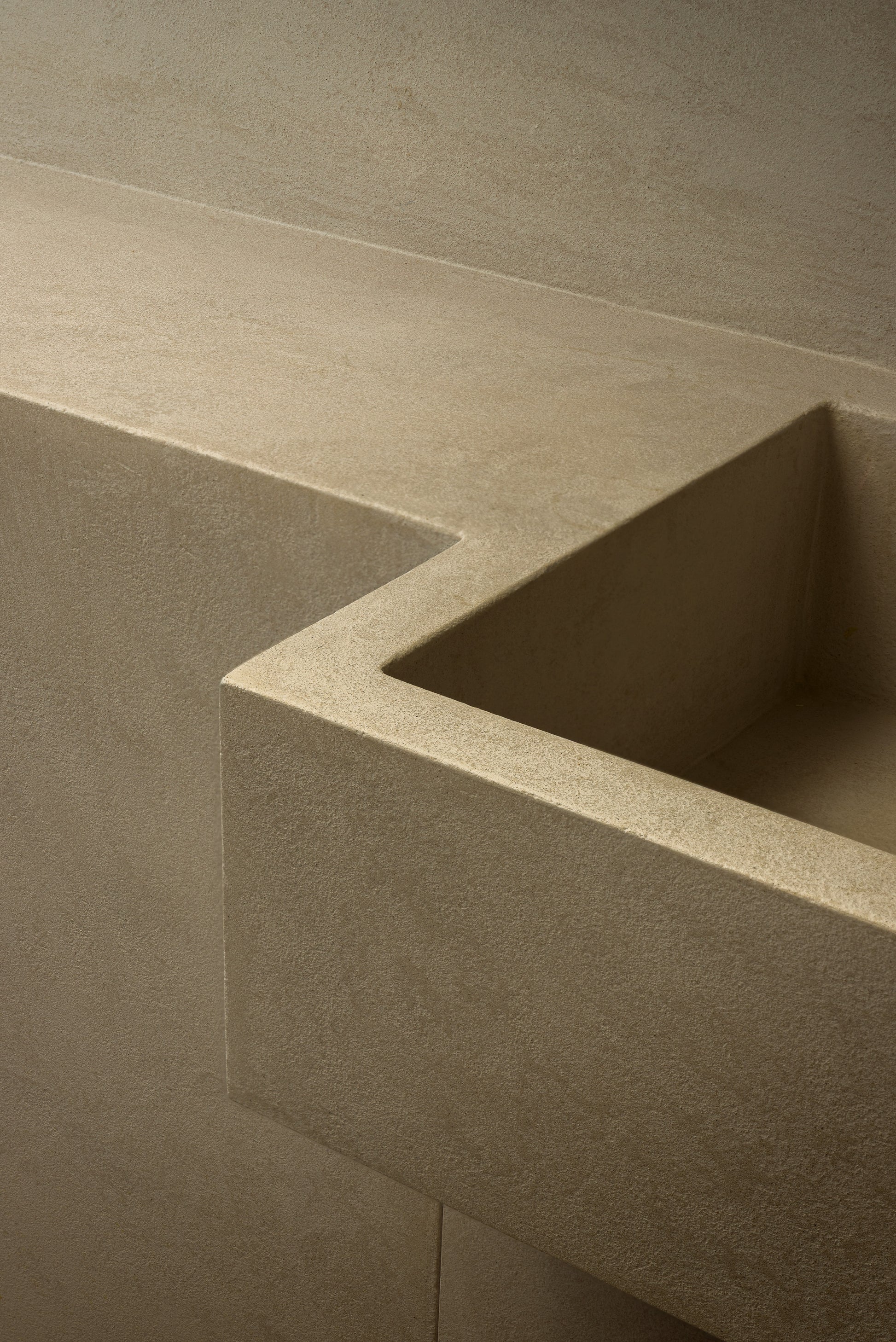 Close-up of a modern L-shaped sink with a thick, textured beige stone or concrete basin and matching wall surface.