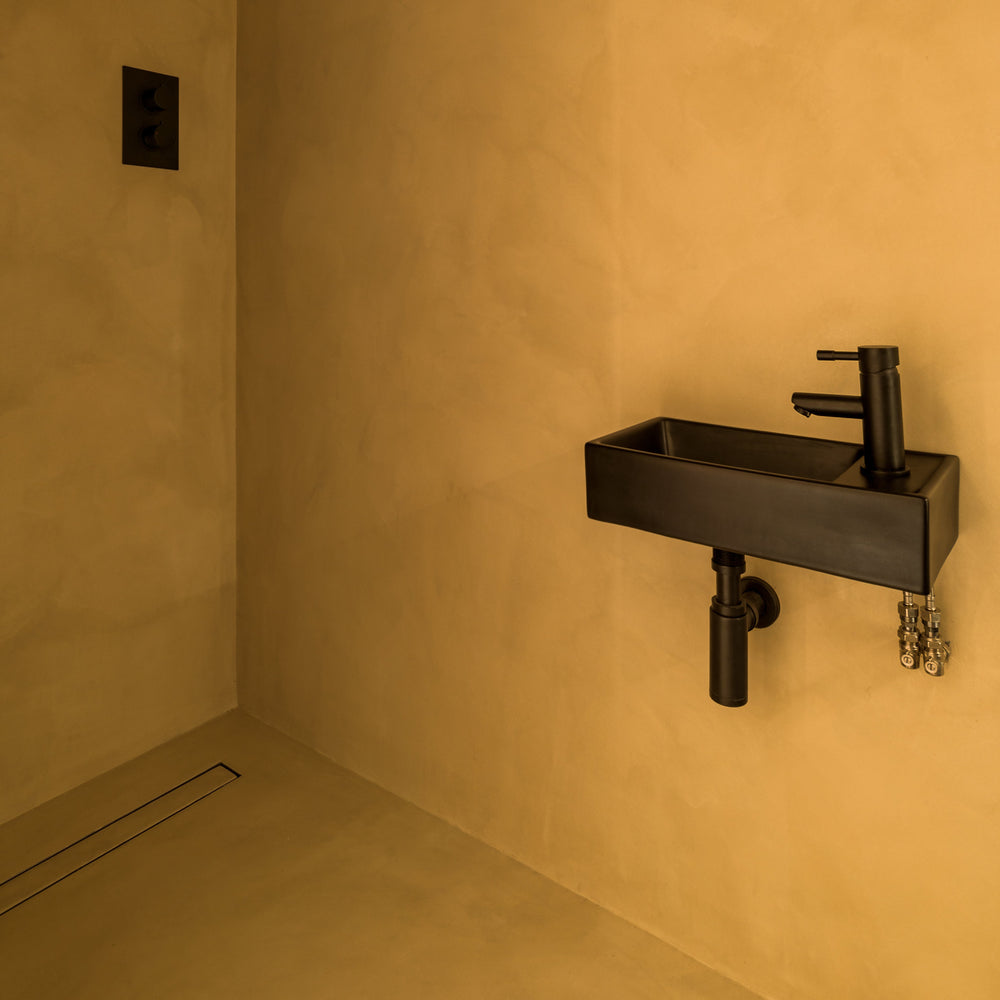 Bathroom corner with a black faucet and sink against a beige wall.