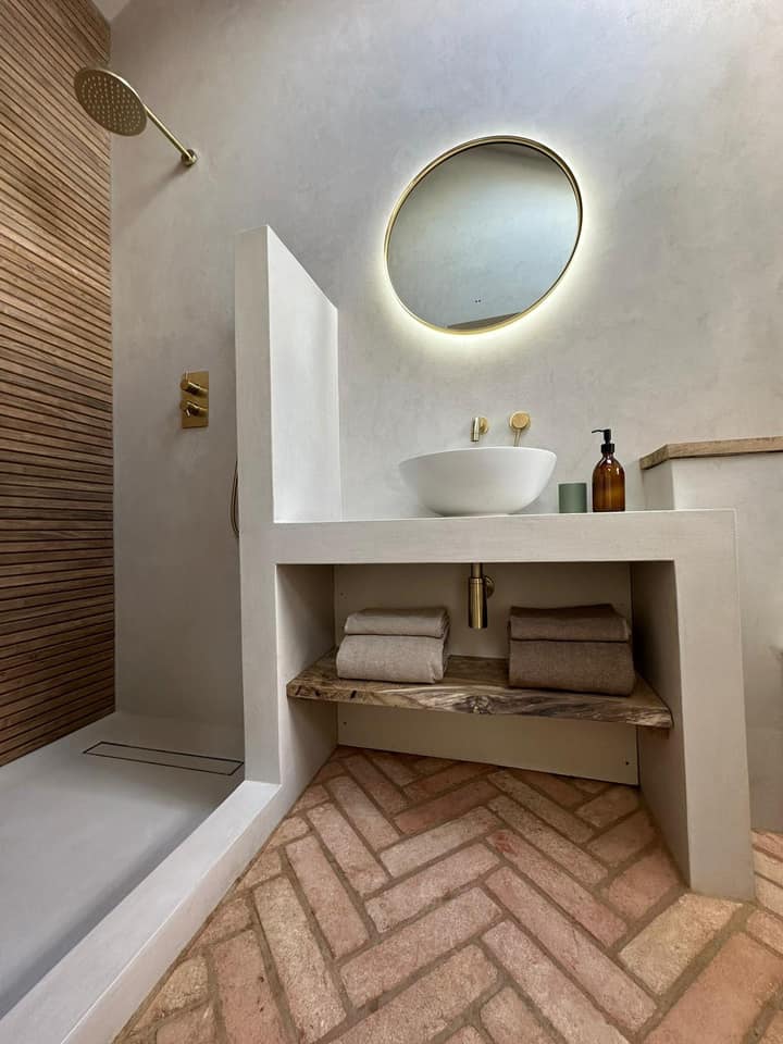 Modern bathroom with concrete vanity, round mirror, and herringbone patterned floor.